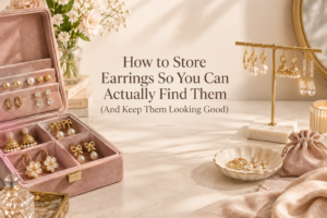 Elegant earring storage setup with stud, hoop, drop, and jhumka earrings organized in a dusty-pink jewelry box, hanging stand, tray, and soft pouch on a warm cream vanity.